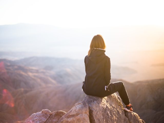 Eine junge Frau sitzt auf einem Felsen und sieht in die Ferne.