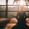 Eine Frau sitzt auf einer Terasse und macht Yoga im Sonnenuntergang